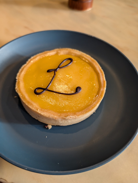 A round lemon tart with a chocolate L on the top