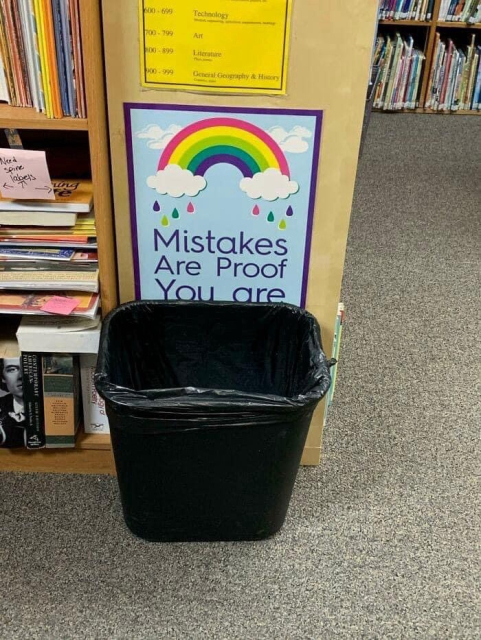 Photo in a library that reads, “Mistakes are proof you are” the rest of the sign is blocked with a trash bin. 