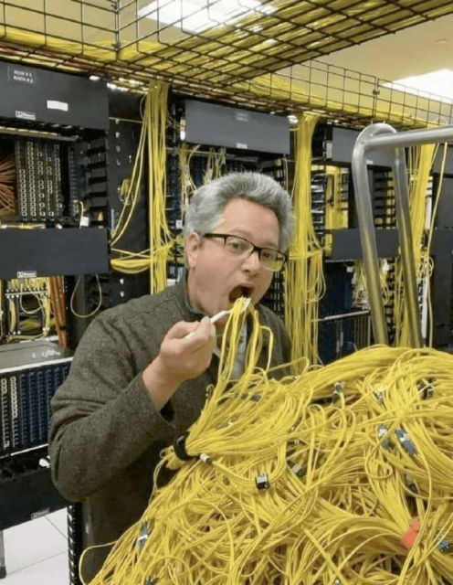 Person in data center pretending to eat yellow cables from a big pile like spaghetti. In the background there are visible racks that use yellow cables