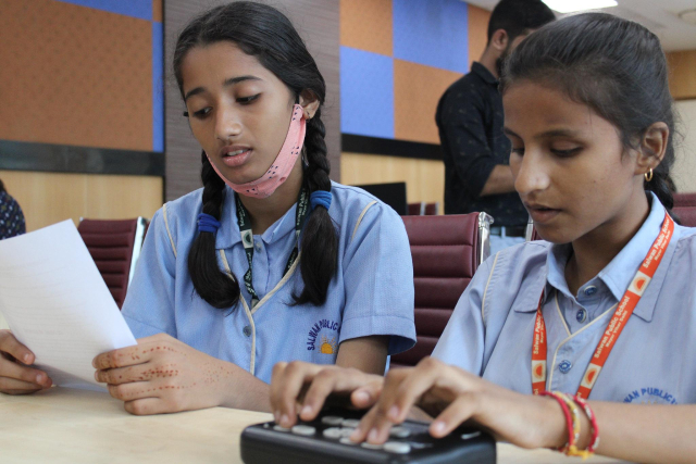 Two girls are sitting on the bench and one of the girls is writing on the Orbit Reader 20 braille display.