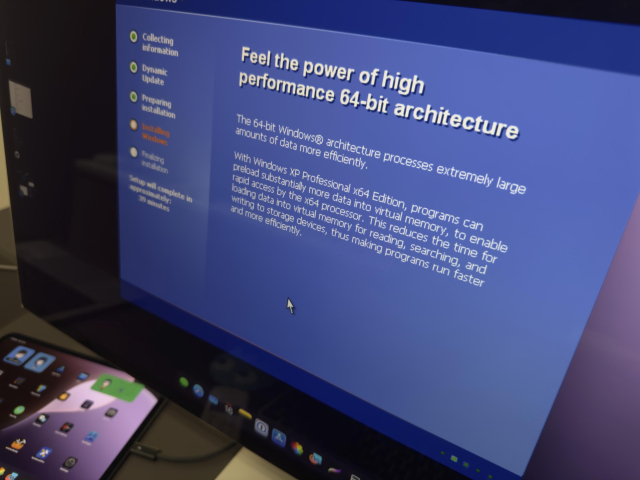 Picture of an iPad Pro connected to a Studio Display. An app is running in the Studio Display showing a Windows XP installation interface with the title “Feel the power of high performance 64-bit architecture”