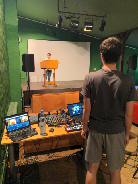 Jonas at the AV console at Regenbogenfabrik. In front of him there's Jordan on the stage.