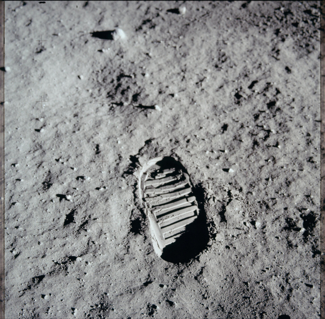 Color photo of a footprint in the lunar surface. It has horizontal treads from the bottom of the astronaut's boot. Despite being a color photo, the image is primarily light gray and black.
