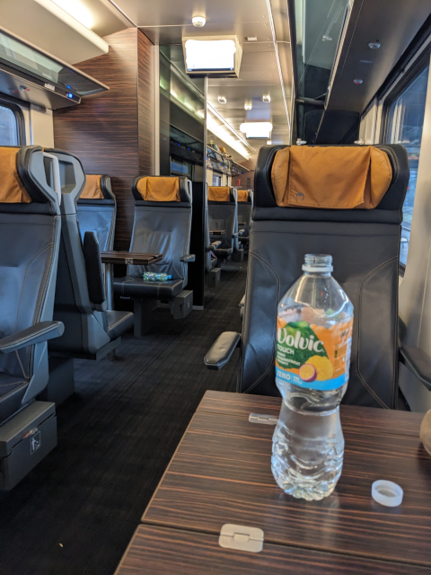 An almost empty, fancy-looking train compartment with leather seats. In front of me is a big bottle of water.