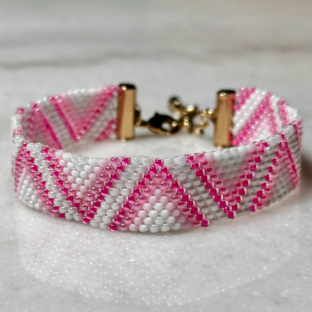 A triangle-patterned pink and white beaded bracelet with a gold clasp  on a marble background