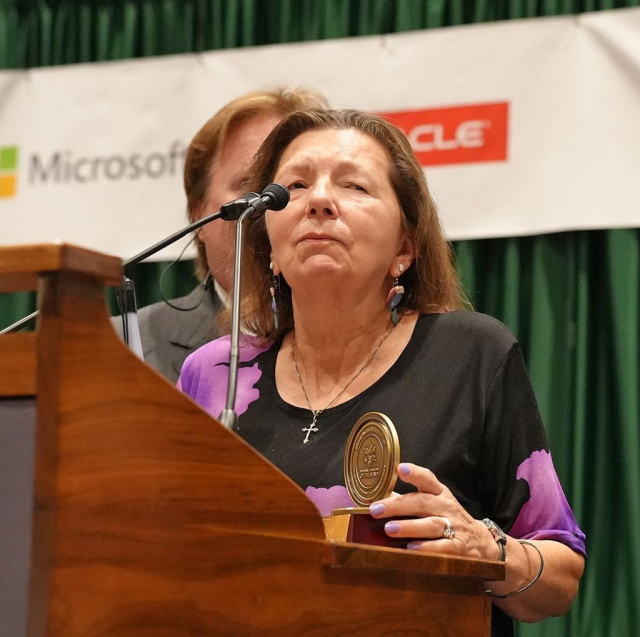 Donna Posont is standing before a podium on stage while holding her Dr. Jacob Bolotin award at the National Convention.