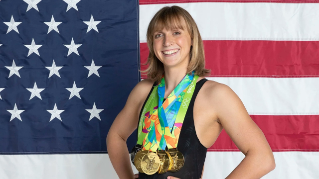 Swimmer Katie Ledecky poses with several Olympic medals in front of a US flag