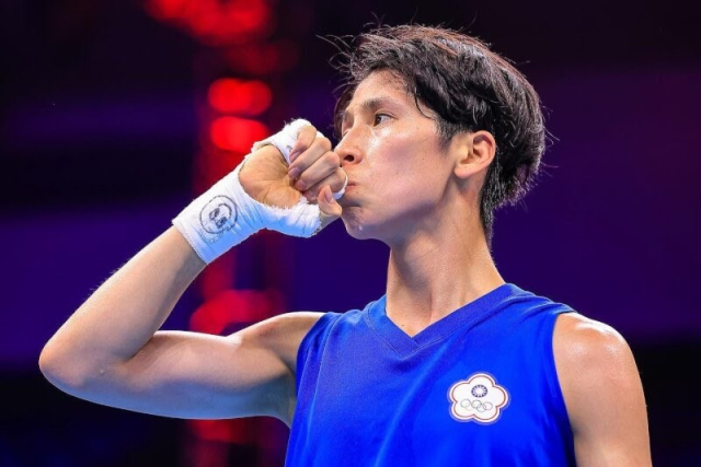 Close shot of Lin Yu-Ting wearing a blue uniform, having raised her fist to her mouth and looking sideways. 