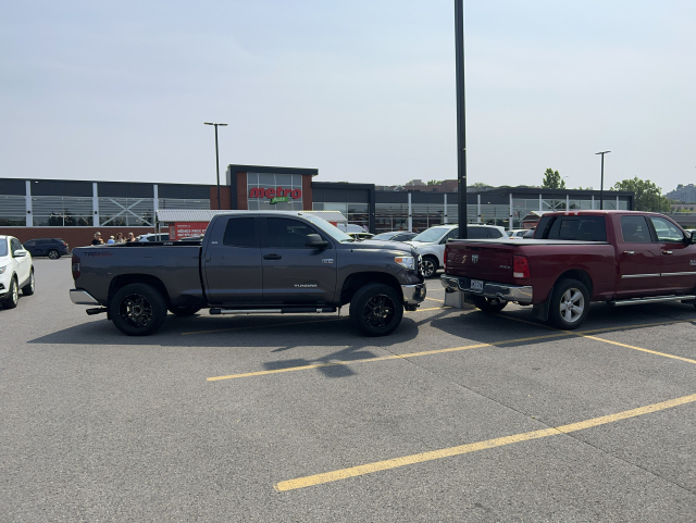 Two pick up trucks parked. The one ahead is hanging out to the spot behind because it’s too big. The one behind is parked diagonally encroaching on the driving lane. Like nothing else matters. Both trucks are huge.