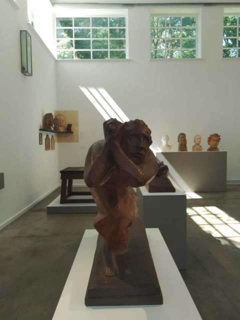 Auf einem weißen Kastenartiken Sockel stehen vor eine weißen Wand 4 lebensgroße Büsten aus unterschiedlichen Materialien: Weißer Gips, Schellackierten Gips und Holz.
An der wand zeichnen die Oberlichte eine geometrisches Lichtbild.