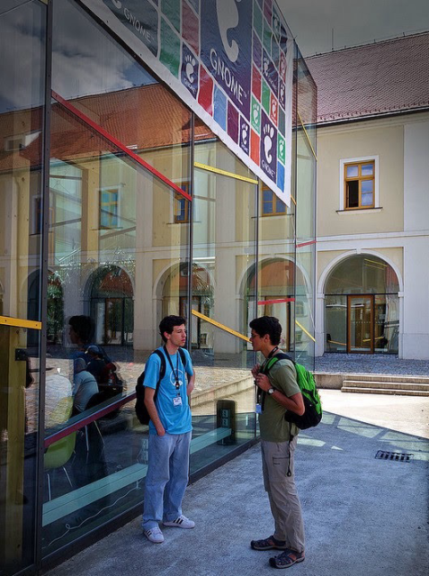 Two happy gnome contributors chatting in front of a colorful gnome banner hanging at a building facade.