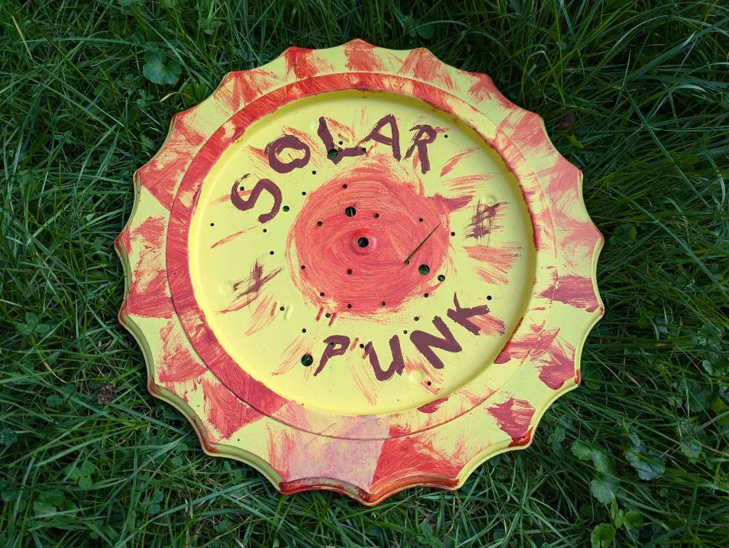 An old part of a lamp was reused and has been painted with a yellow sun with red flames and the words solar punk