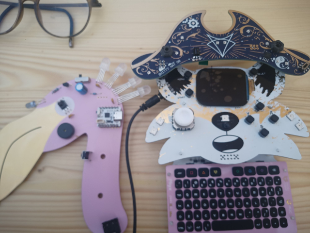 Various electronic devices: the fox-badge of Fri3d-camp, with communicator addon and a pirate hat (shitty add on by the Coderdojo-village) and the flamingo-blaster