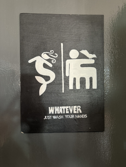 The sign shows a mermaid on the left and the center on the right with the bird on its arm. Below that it simply says, "WHATEVER
JUST WASH YOUR HANDS"