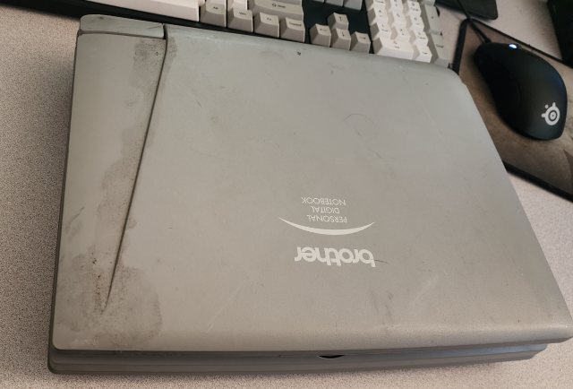 A grey thick laptop from the 90s, with "brother personal digital notebook" on top. it's got some grime on the left side