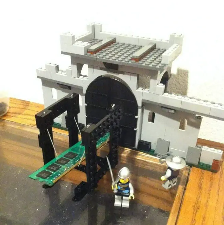 A fortress made of Lego. Outside are two Lego men with a swinging battering ram in black, but with the wooden part replaced by a green RAM memory stick