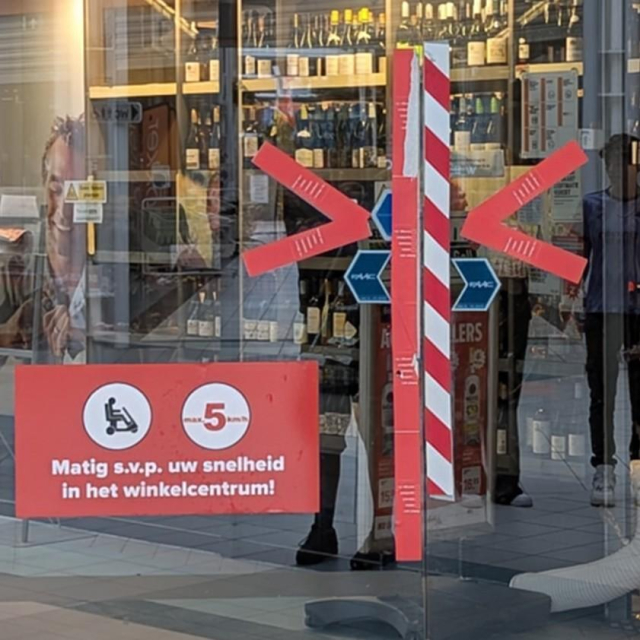 A glass sliding door with edges covered by red and white tape. On the left there's a big sign with an icon of a mobility scooter and text "max 5 km/h".