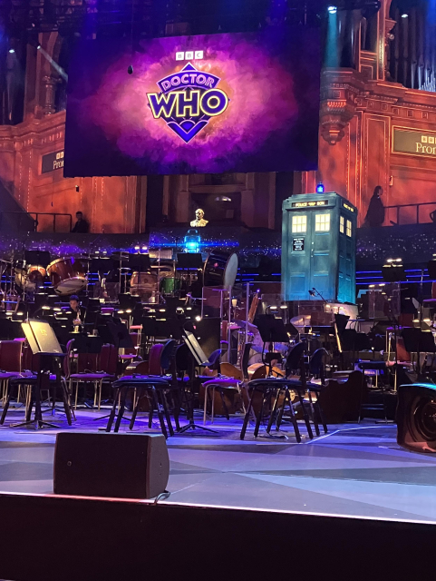 The stage at the Royal Albert Hall, with the orchestra seats, the TARDIS, and a large scrrrn showing the latest Doctor Who logo