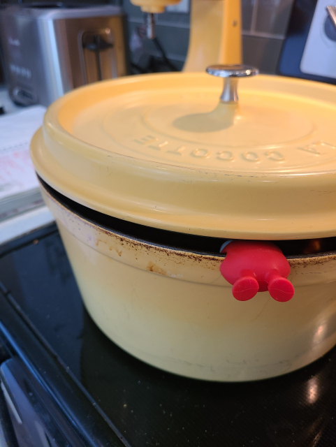 A Dutch Oven on the stove, with the lid on. The lid is held slightly ajar by a small monster, whose feet are the only thing visible outside the pot.