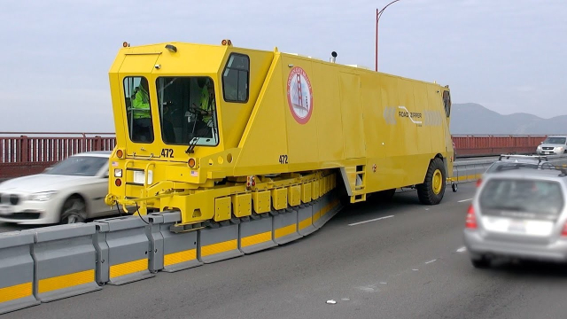 an image of a large utility vehicle on the golden gate bridge. it is functionally a giant, two-ended truck that operates as a zipper for the articulated median barrier, allowing the bridge's operators to swap it from one side of the middle lane to the other.