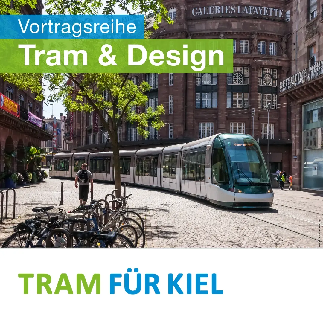 Eine lange Tram mit großen Fenstern fährt über eine mit Natursteinen gepflasterte Straße. Sie schlängelt sich durch die recht enge Straße, die von mehrgeschossigen Bauten aus dem 19. Jahrhundert umgeben ist.