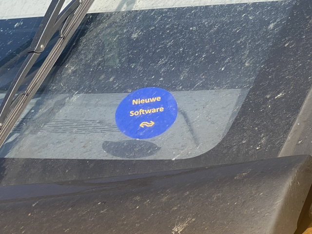 A blue round sticker on a windscreen with the yellow text “Nieuwe Software” and the NS logo below.