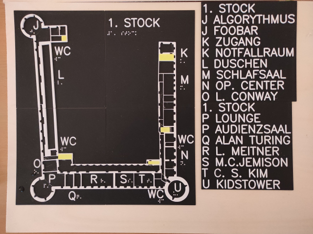 Taktiler Plan vom Håck ma's Castle. Grundriss des 1. Stocks des Schlosses in Ottenschlag, mit vier runden Ecktürmen, West-, Süd- und Osttrakt. Orte am Plan sind mit Buchstaben in taktiler Profilschrift und Brailleschrift markiert. Eine Legende in Profilschrift erklärt die Bedeutung der Buchstaben am Plan. Weiße Zeichnung und Schrift sowie gelb markierte Räume auf schwarzem Grund auf einer Holzplatte.