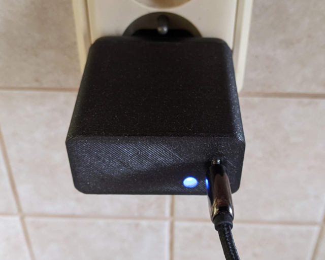 A USB power supply with a 3D printed cover. Next to the USB socket blue light shines through the cover.