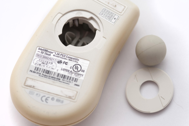 An old style mouse turned upside down, the tracking ball compartment is open and the ball is removed for cleaning.