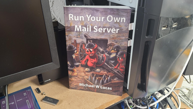 A copy of the paperback book "Run Your Own Mail Server" by Michael W. Lucas, propped up in front of a black mid-tower computer that just so happens to be acting as my personal email server.