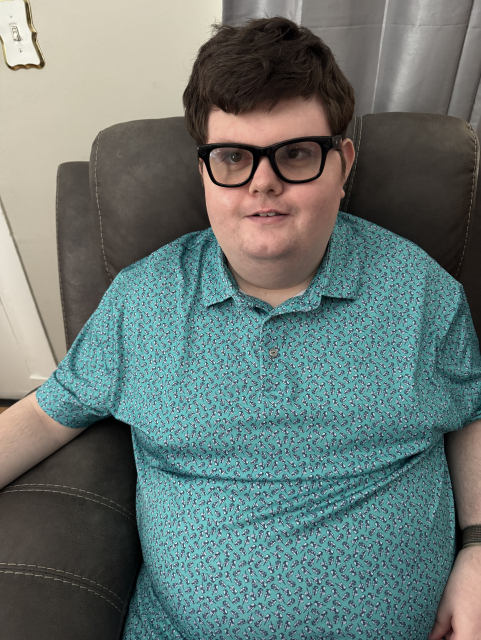 Cullen sits in a chair wearing black Meta smart glasses and a teal patterned polo shirt, smiling for the camera.