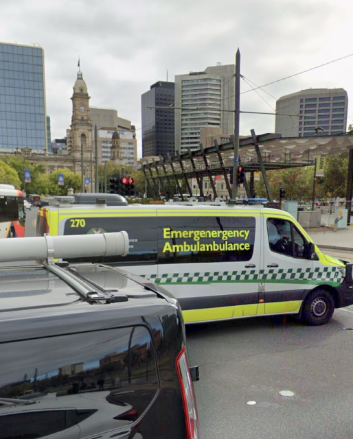 A Google Street view screen grab, showing a white Mercedes Sprinter Van Ambulance, with yellow high visibility stickers and green/white checkered pattern. There is a distortion where two images are blended, stretching the vehicle’a length and causing the words “emergency ambulance” to appear as they did in my toot. 