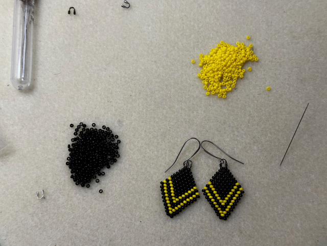 A bead board with black and yellow beads and a pair of black diamond shaped beaded earrings with yellow chevron stripes