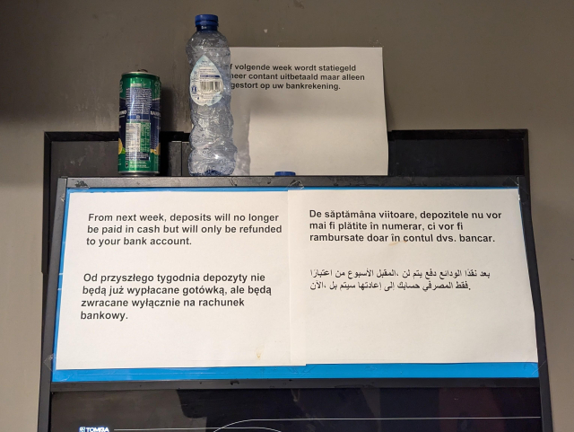 A part of TOMRA reverse vending machine with signs in 5 languages: 

"From next week, deposits will no longer be paid in cash but will only be refunded to your bank account."