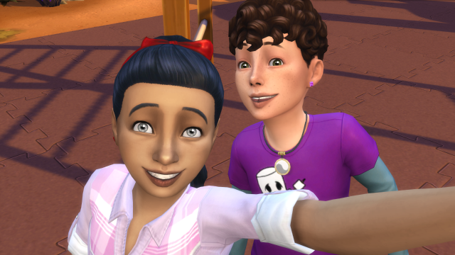 Screenshot from The Sims 4, showing two kids - a girl with black hair and grey eyes, and a boy with curly brown hair and green eyes, taking a selfie on a playground.