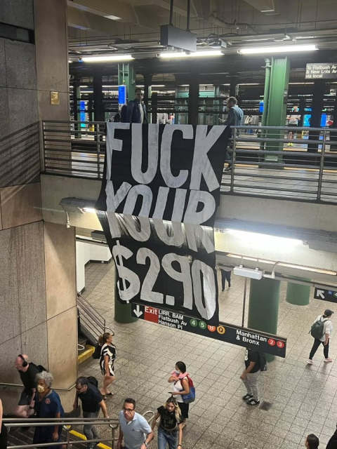 photo taken inside an NYC subway station. there is a huge banner hung from an upstairs railing that reads

FUCK YOUR $2.90