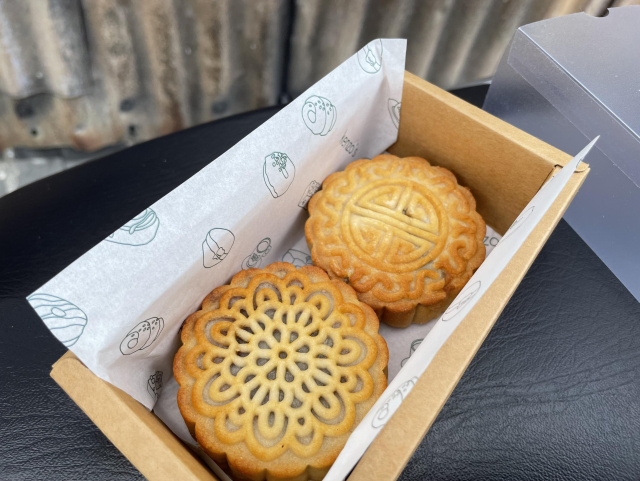 Two mooncakes in a box. On a black bench (its actually my scoter seat). Next to a tin shed. 