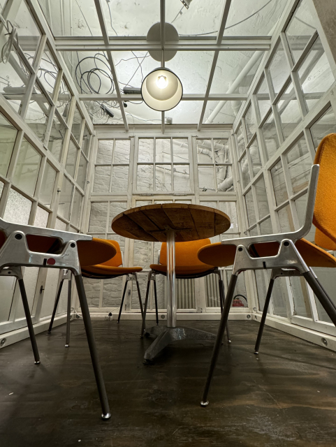 A small glass room with orange chairs and a small table