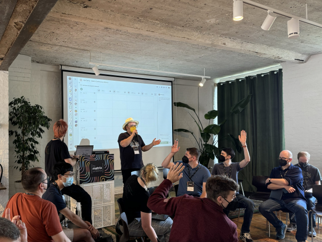 A picture of a speaker asking a question and a crowd raising hands. In the background there’s a matrix widget to build a barcamp schedule