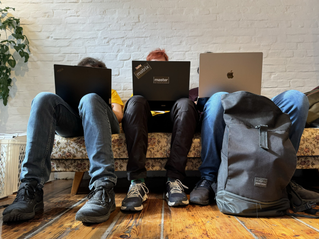 A picture of three people sitting in a vintage sofa next to each other. Their face is hidden behind their laptop lids.