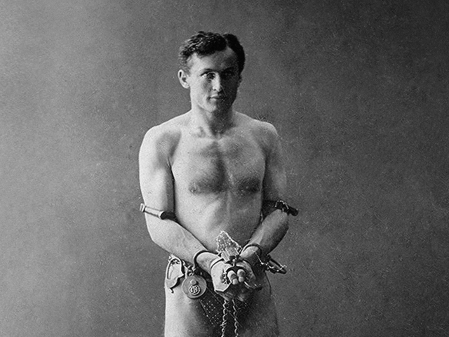 Mostly naked Houdini, he got that sleeper body, he's wearing a fur loin cloth and he's all chained up