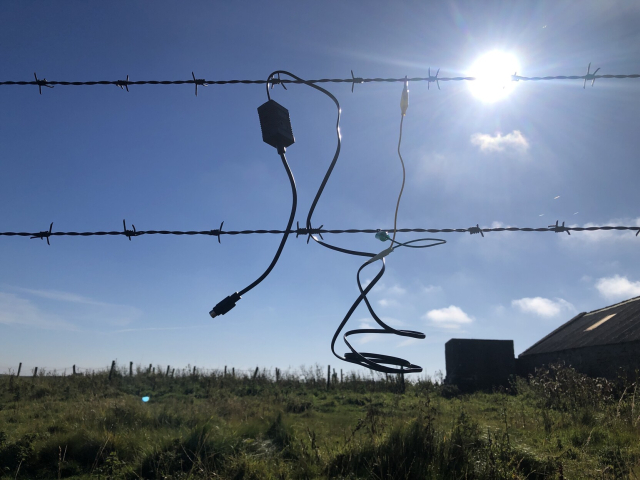 A phonenet connector and some alligator clips hanging from some barbed wire