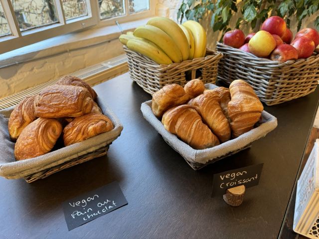 A picture of pastries on a table with fruit baskets. There are two labels: “Vegan pain au chocolat” and “vegan croissant”