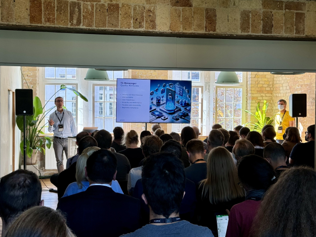 A picture of a male speaker in front of a massive crowd in a packed room