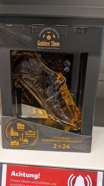 a bottle of blended scotch whiskey in the shape of a football cleat sitting on a store shelf. the brand name is Golden Shoe