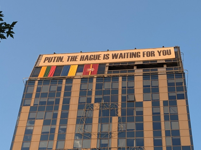 A picture of the top of a skyscraper with a transparent reading: "PUTIN, THE HAGUE IS WAITING FOR YOU"
Underneath, the flags of Lithuania, Ukraine and Vilnius are hanging.