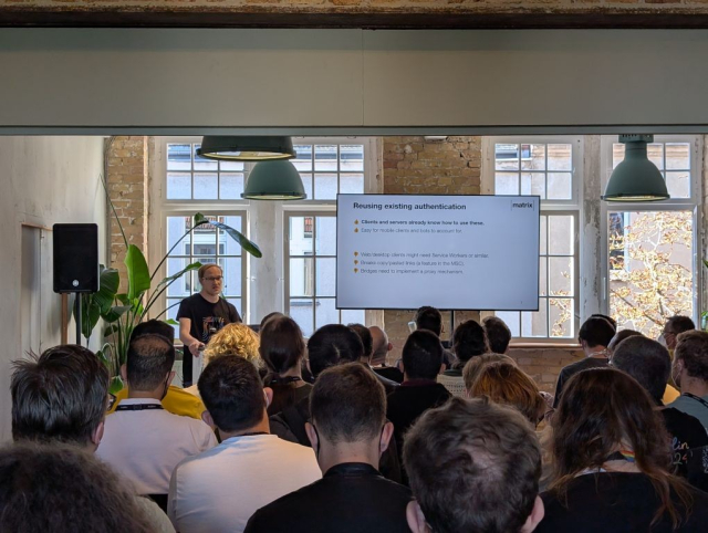 A picture of a room full of people and the speaker Travis Ralston giving their talk 