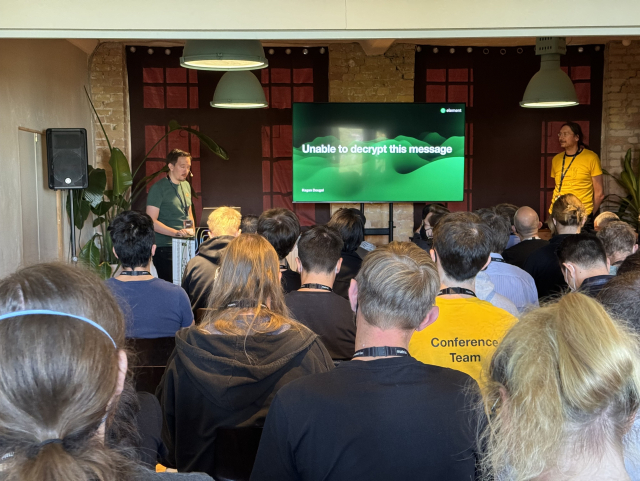 A picture of a speaker in front of a large crowd. His first slide reads “Unable to decrypt this message”