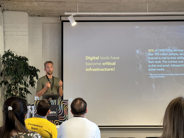 A picture of the speaker, Emil, presenting their slides. The slides read “Digital tools have become critical infrastructure!”