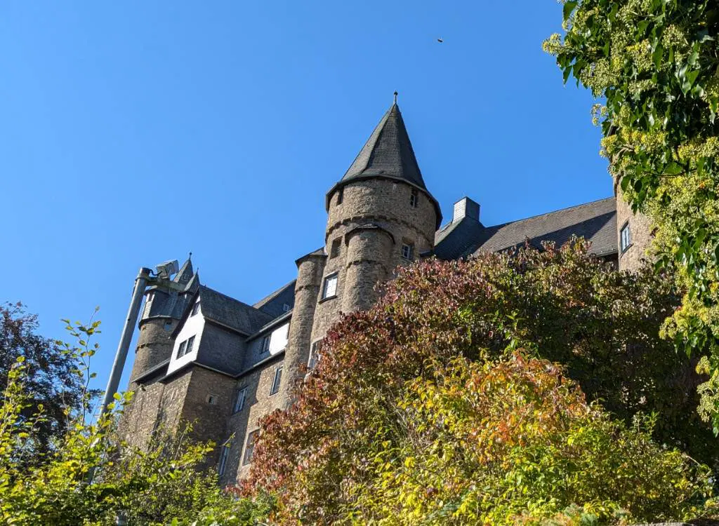 Ein Teil des Schlosses Herborn von unten mit zwei Türmen fotografiert. Davor herbstlich gefärbtes Laub, blauer Himmel im Hintergrund.